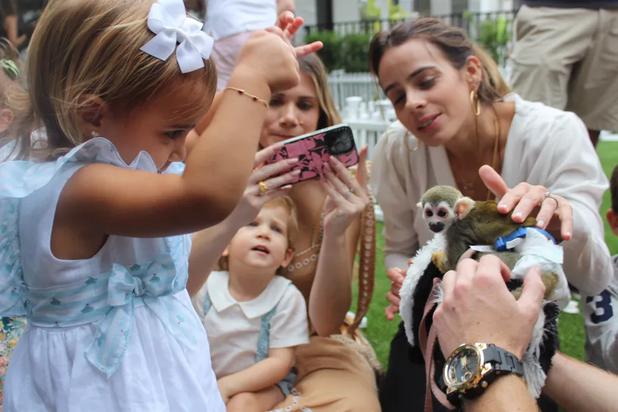Guests at an elegant garden party photographing a squirrel monkey held by a handler